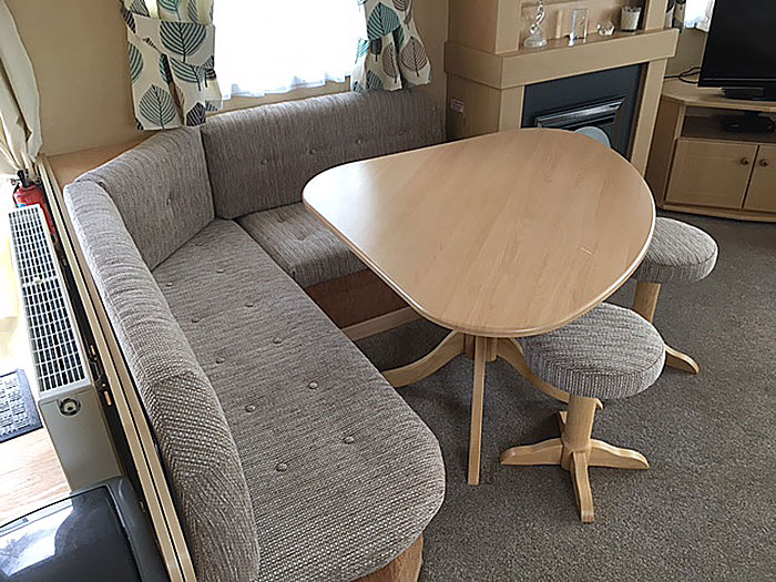 A re-upholstered static caravan seating area, with buttoned cushions and matching stool upholstery 